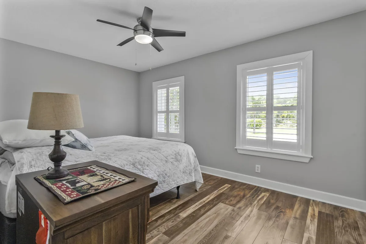 Bedroom staged with a bed, nightstand and lamp beside plantation-shuttered windows