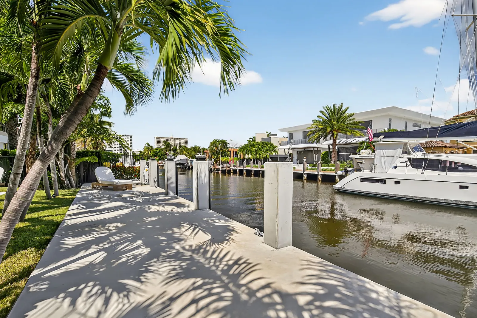 Private dock on a canal with a yacht moored and palm shadows across the deck