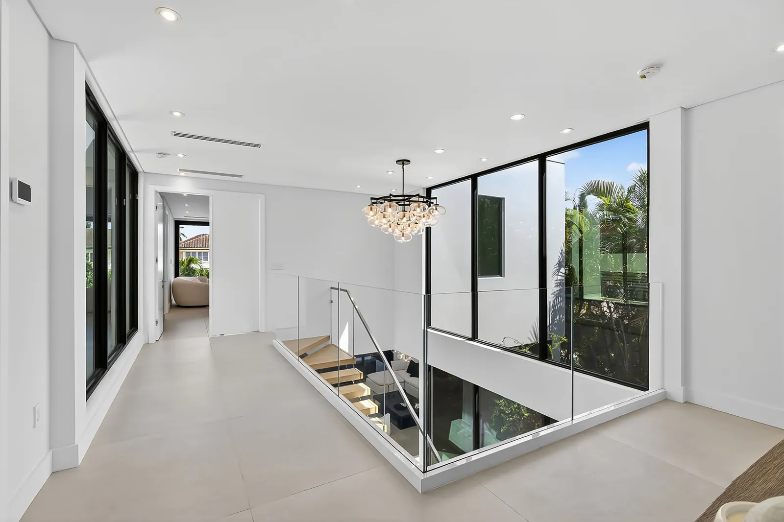 Upstairs landing with a glass stair rail, chandelier and floor-to-ceiling windows
