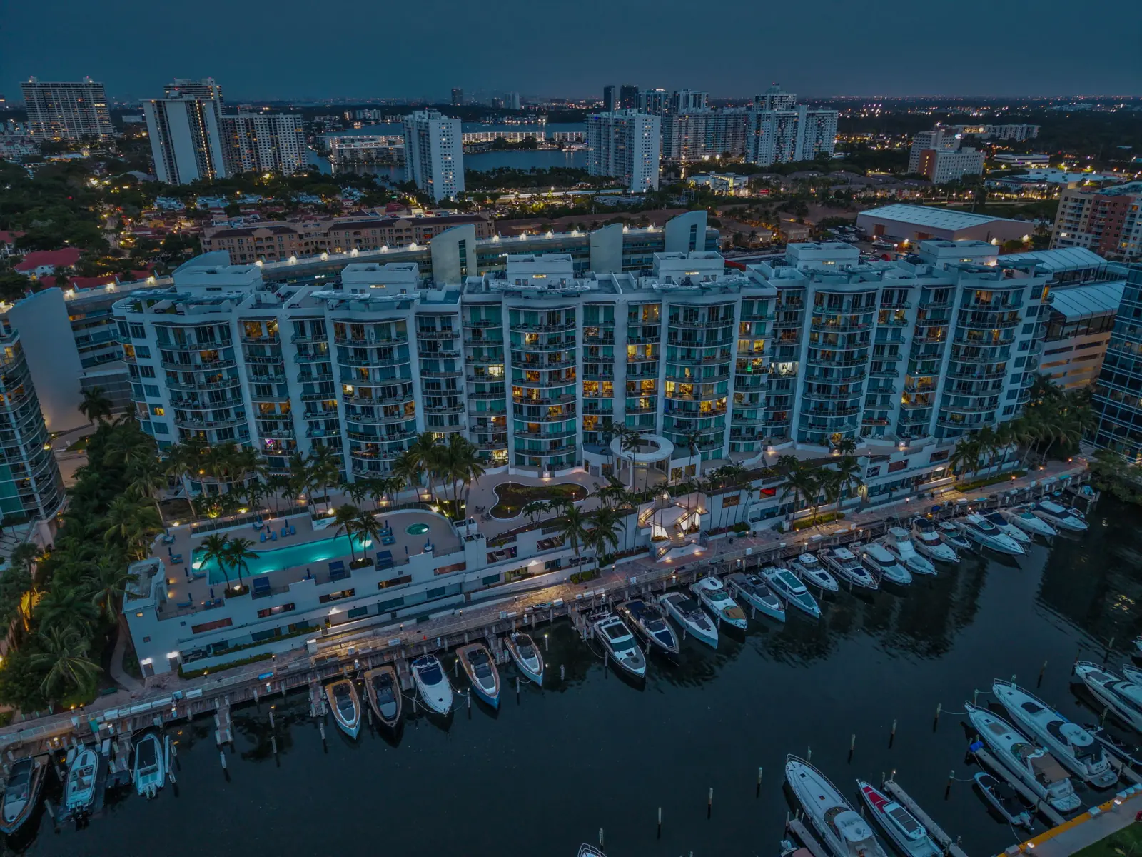 Dusk aerial of an Aventura waterfront condo with pool deck and marina