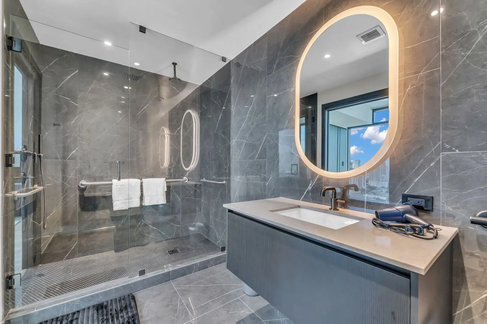 Marble condo bathroom with lit oval mirror in Miami